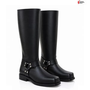 May include: A pair of black knee-high leather boots featuring a square toe, a low heel, and a decorative harness strap across the ankle secured with silver-toned metal rings and rivets. The Morar Leather Gear logo is visible in the top right corner.