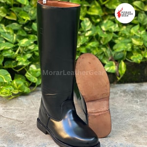 May include: Black leather riding boots with a shiny finish. One boot is upright, and the other is lying on its side, revealing the sole. The boots are tall, reaching the knee, and have a classic design.