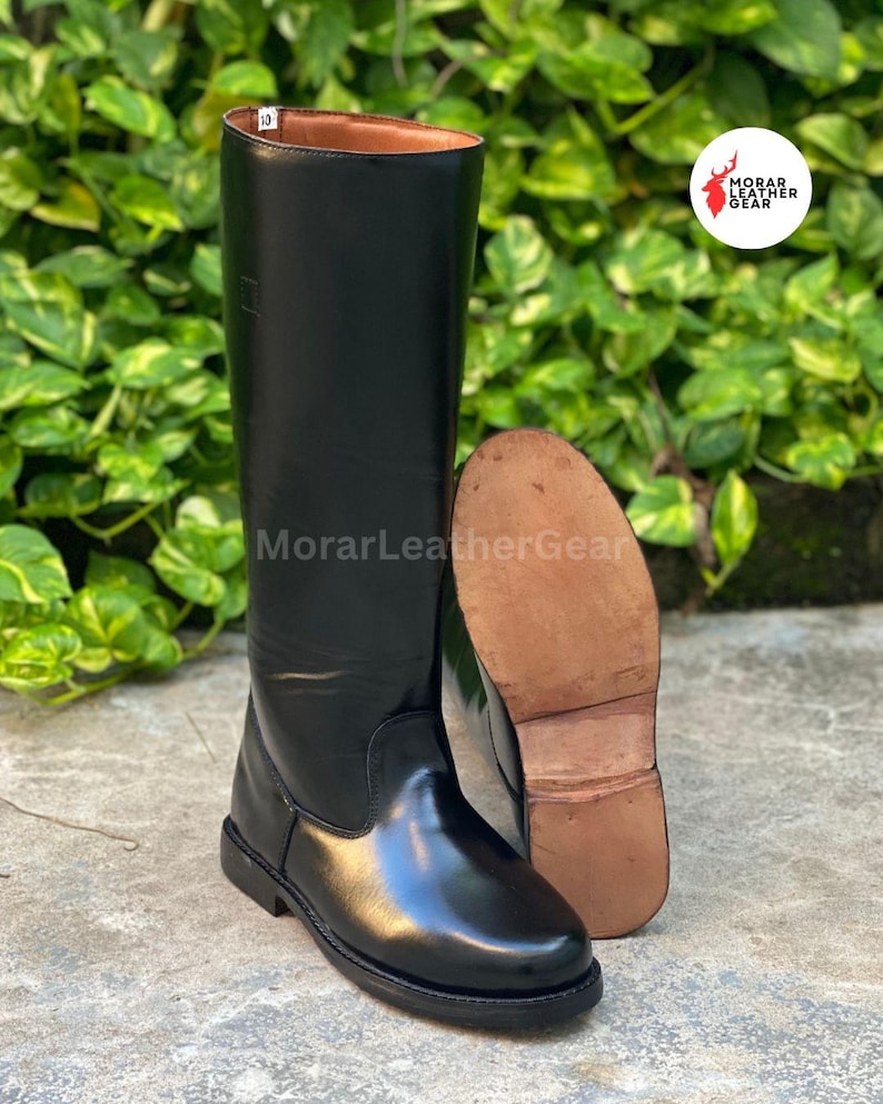 May include: Black leather riding boots with a shiny finish. One boot is upright, and the other is lying on its side, revealing the sole. The boots are tall, reaching the knee, and have a classic design.