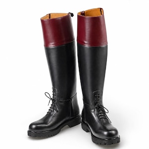 May include: A pair of knee-high boots featuring a black leather lower section with front laces and a contrasting deep burgundy leather cuff at the top. The boots have a thick, lugged black rubber sole and a tan interior lining. Logo reads MORAR LEATHER GEAR.