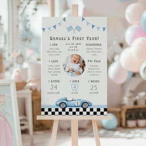 May include: A light-colored sign on an easel, featuring the text "Samuel's First Year!" with a photo of a baby. The sign includes the baby's height (24 inches), weight (25 pounds), and favorite foods. A blue race car graphic is at the bottom.
