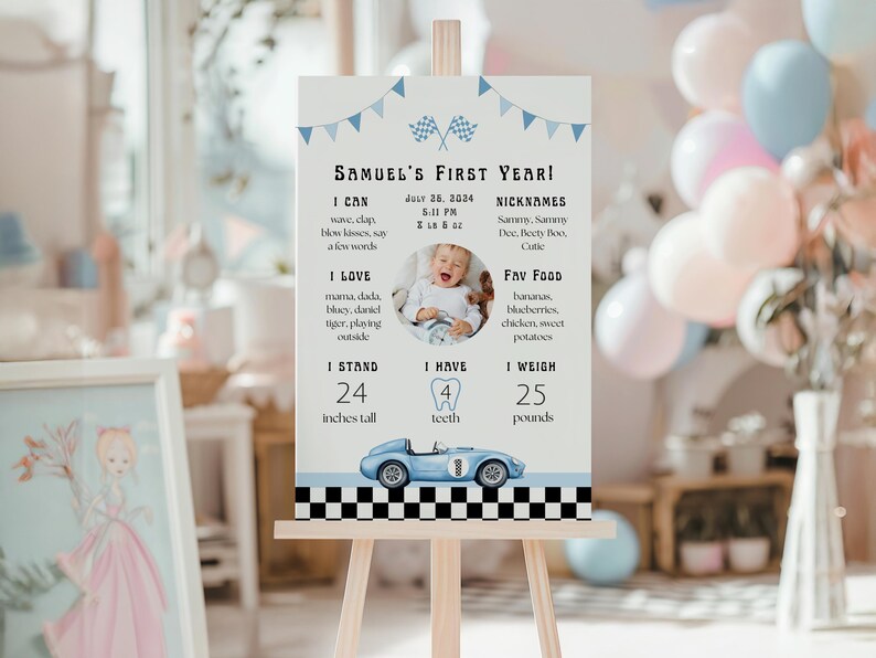 May include: A light-colored sign on an easel, featuring the text "Samuel's First Year!" with a photo of a baby. The sign includes the baby's height (24 inches), weight (25 pounds), and favorite foods. A blue race car graphic is at the bottom.