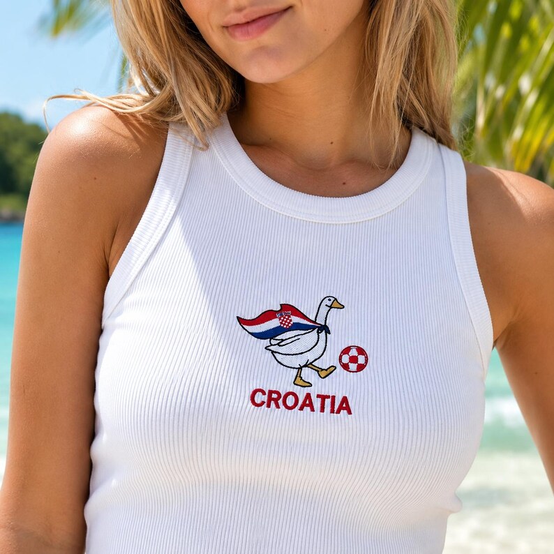 May include: A white ribbed tank top featuring an embroidered graphic of a white goose wearing a cape with the red, white, and blue Croatian flag pattern. The goose is kicking a red and white checkered soccer ball, with the word CROATIA in red.