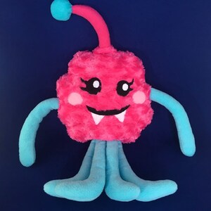 Puede incluir: Un monstruo de peluche rosa con una antena azul, brazos azules y piernas azules. El monstruo tiene una cara amigable con ojos negros, mejillas rosadas y dientes blancos.