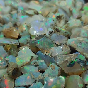 Op de afbeelding: Een close-up van een stapel ruwe opaal edelstenen. De opalen zijn een mix van wit, helder en bruin, met flitsen van iriserende kleur. De edelstenen zijn ongesneden en hebben een natuurlijke, ruwe uitstraling.