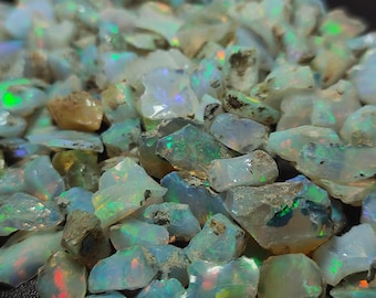 May include: A close-up of a pile of rough opal gemstones. The opals are a mix of white, clear, and tan, with flashes of iridescent colour. The gemstones are uncut and have a natural, raw appearance.