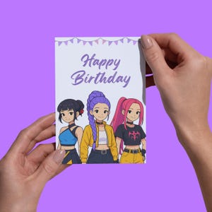 Op de afbeelding: Een wenskaart met de tekst "Happy Birthday" in paarse letters. De kaart toont een illustratie van drie meisjes in anime-stijl met verschillende kapsels en outfits. De achtergrond is lichtpaars met kleine bannerversieringen.