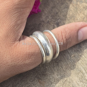 May include: Three silver rings of different widths are stacked on a finger. The rings have a polished, reflective surface. The text "BalajisilverartIN" is visible on the image. The rings are likely part of a jewelry collection.