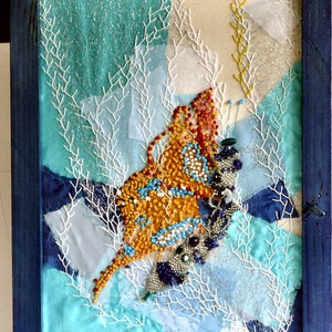 Op de afbeelding: Een ingelijst kunstwerk met een kleurrijke vlinder gemaakt van kralen en pailletten, tegen een achtergrond van blauwe en witte stof met een glinsterende textuur.