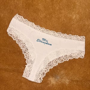 May include: White underwear with delicate lace trim. The text "Mrs. Etringham" is embroidered in a teal color on the front. The underwear is made of a soft, ribbed fabric.
