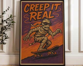 May include: A framed rectangular wall art print featuring a mummy wearing sunglasses and riding a skateboard. The text CREEP IT REAL is printed in orange at the top. The background consists of orange and purple sunset-like colour gradients.