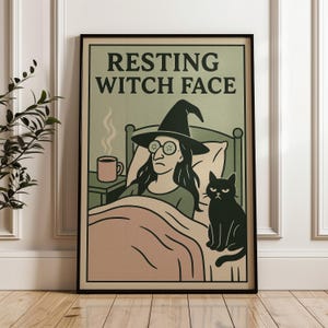 May include: A framed poster with the text "RESTING WITCH FACE" above an illustration of a witch in bed with a black cat. The witch wears a hat and glasses with cucumber slices. A mug of coffee sits on a nightstand.