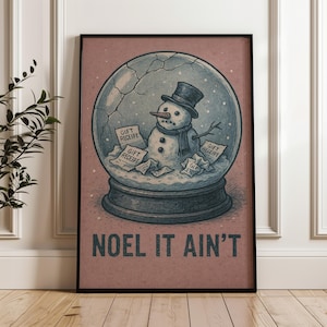 May include: Framed art print depicting a snowman in a snow globe. The snowman is wearing a top hat and scarf, with gift receipts scattered around. The text "NOEL IT AIN'T" is printed below, set against a pink background.
