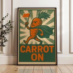 May include: A rectangular poster in a black frame featuring a stylised orange carrot character with a green cape and leafy top, running while holding an orange flag. The background has green and cream sunburst rays, with the text CARROT ON below.