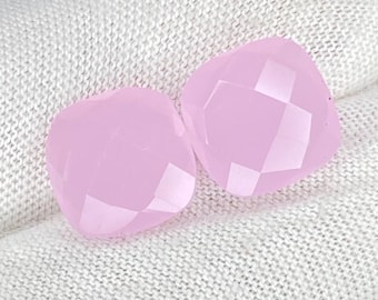 May include: Two square-shaped, faceted light pink gemstones with rounded corners. The stones feature a polished, reflective surface with geometric cuts that create a symmetrical pattern across the top faces, showcasing a soft, translucent pastel hue.