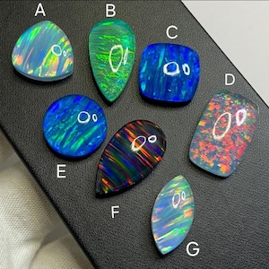 May include: A collection of seven opals in various shapes, including teardrop, oval, and square. The opals display a range of colors, such as blue, green, orange, and red, with iridescent patterns. Each opal is unique, showcasing natural variations in color and pattern.