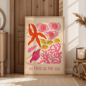 Könnte beinhalten: Ein gerahmter Kunstdruck mit einem maritimem Design. Das Kunstwerk zeigt einen leuchtend orangefarbenen Seestern, rosa Fische, gelbe Fische, Korallen und Muscheln. Der Text "AS FREE AS THE SEA" ist unten auf dem Druck abgebildet.