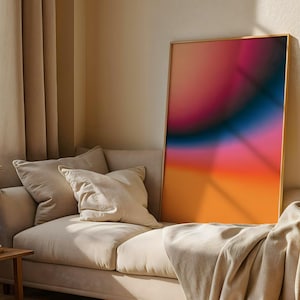 Könnte beinhalten: Ein gerahmter abstrakter Kunstdruck mit einem Farbverlauf aus Orange, Pink, Blau und Lila. Das Kunstwerk wird auf einem beigen Sofa mit Kissen und einer Decke präsentiert. Der Raum hat beige Vorhänge und einen hölzernen Beistelltisch.