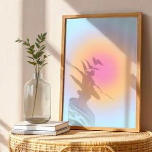 Puede incluir: Una impresi&oacute;n art&iacute;stica enmarcada con un dise&ntilde;o abstracto suave y colorido. La obra de arte presenta un degradado de tonos rosas, naranjas y azules. Un jarr&oacute;n de vidrio transparente con tallos y hojas verdes se encuentra sobre una mesa tejida, junto a una pila de libros.
