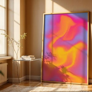 Könnte beinhalten: Ein gerahmter Kunstdruck mit einem lebendigen, abstrakten Design. Das Kunstwerk zeigt eine Mischung aus Rosa, Orange und Lila, die eine dynamische und farbenfrohe Komposition erzeugt. Der goldene Rahmen verleiht dem Stück eine elegante Note, ideal für die Inneneinrichtung.