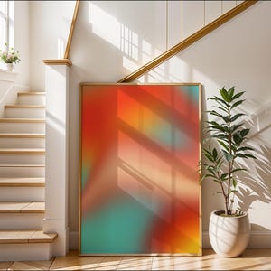 Può includere: Una grande stampa artistica astratta incorniciata con una vibrante miscela di colori rosso, arancione e verde acqua. L'opera d'arte è esposta contro un muro bianco, accanto a una pianta in vaso. La stampa è in una cornice di legno.