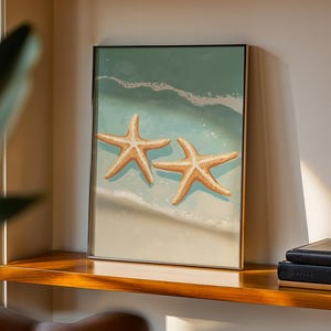 Könnte beinhalten: Ein gerahmter, rechteckiger Wandkunstdruck, der zwei hellbraune Seesterne an einem Sandstrand zeigt, mit türkisfarbenem Meerwasser und weißen Schaumkronen, die in einer klaren, hellen und detaillierten Küstenillustration über den Sand spülen.