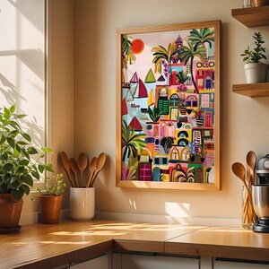 May include: A colorful framed artwork depicting a coastal town scene with buildings, sailboats, and palm trees. The artwork features a vibrant palette of reds, blues, greens, and yellows. The artwork is displayed in a kitchen setting with wooden shelves and utensils.