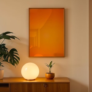 May include: A modern interior scene featuring a wooden cabinet, a glowing orb lamp, and a framed abstract art piece with an orange gradient. A potted plant and a small succulent in an orange pot add a touch of nature to the room.