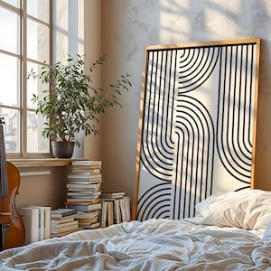 Könnte beinhalten: Ein Zimmer mit einem großen, gerahmten Kunstwerk mit einem schwarz-weißen geometrischen Design. Ein Cello lehnt an einem Fenster, und eine Topfpflanze steht auf einer Fensterbank. Ein Stapel Bücher und ein Bett mit einer weißen Bettdecke sind ebenfalls zu sehen.