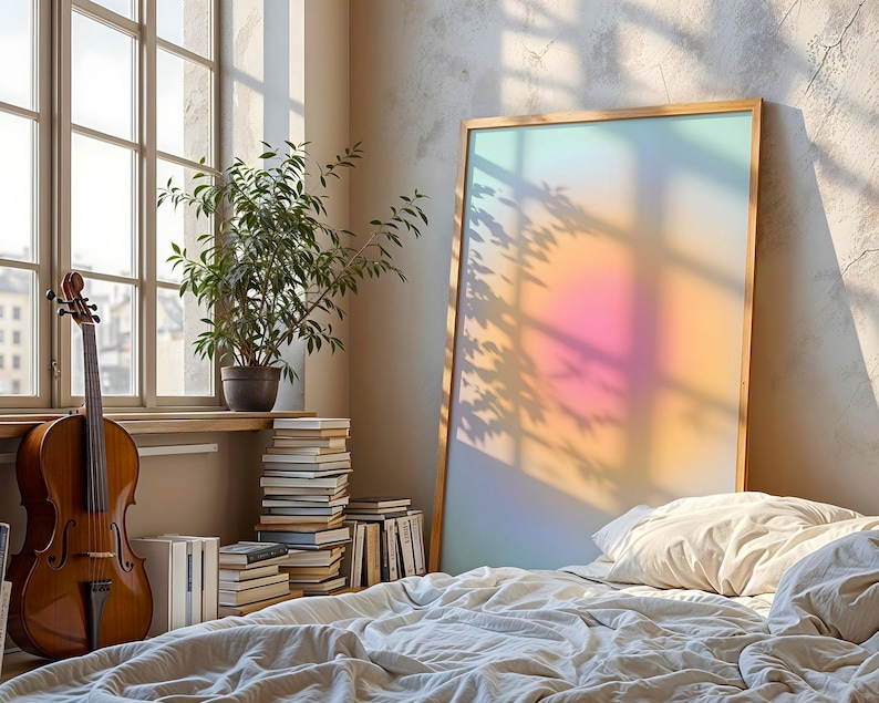 Puede incluir: Una escena de dormitorio con un violonchelo, libros y una gran obra de arte enmarcada. La obra de arte tiene un degradado de color suave. Una planta en maceta est&aacute; en un alf&eacute;izar. La cama est&aacute; hecha con un edred&oacute;n y almohadas blancos.