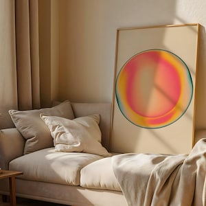 Könnte beinhalten: Ein gerahmter Kunstdruck mit einem abstrakten, farbenfrohen kreisförmigen Design. Das Kunstwerk zeigt einen Farbverlauf aus Rosa, Gelb und Türkis. Der Druck befindet sich auf einem beigefarbenen Hintergrund, mit einem goldenen Rahmen, und ist auf einem beigen Sofa platziert.
