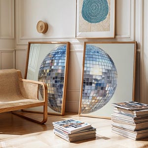 Könnte beinhalten: Zwei gerahmte Drucke mit einem Discokugel-Design. Die Drucke haben einen Holzrahmen und lehnen an einer weißen Wand. Ein Webstuhl und Stapel von Zeitschriften befinden sich im Vordergrund. Ein kreisförmiges Kunstwerk hängt an der Wand.