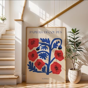 Könnte beinhalten: Ein gerahmter Kunstdruck mit einem floralen Design aus roten Mohnblumen und blauen Stielen auf cremefarbenem Hintergrund. Die Texte „PAPIERS DÉCOUPÉS“ und „POPPIES“ sind auf dem Kunstwerk aufgedruckt. Der Druck wird in einem hellen, gut beleuchteten Innenraum ausgestellt.