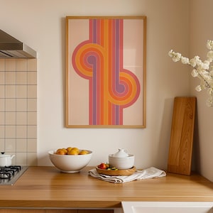 Op de afbeelding: Een ingelijste retro kunstprint met een ontwerp van oranje, roze en paarse gebogen lijnen. Het kunstwerk hangt boven een houten aanrecht met een fruitschaal, een snijplank en een witte keramische kom.