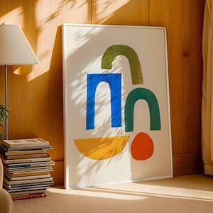 Könnte beinhalten: Ein gerahmter Kunstdruck mit einem abstrakten Design auf weißem Hintergrund, mit blauen, grünen, orangefarbenen und gelben geometrischen Formen. Das Kunstwerk lehnt an einer Holzwand, mit einer Lampe und Büchern im Hintergrund.
