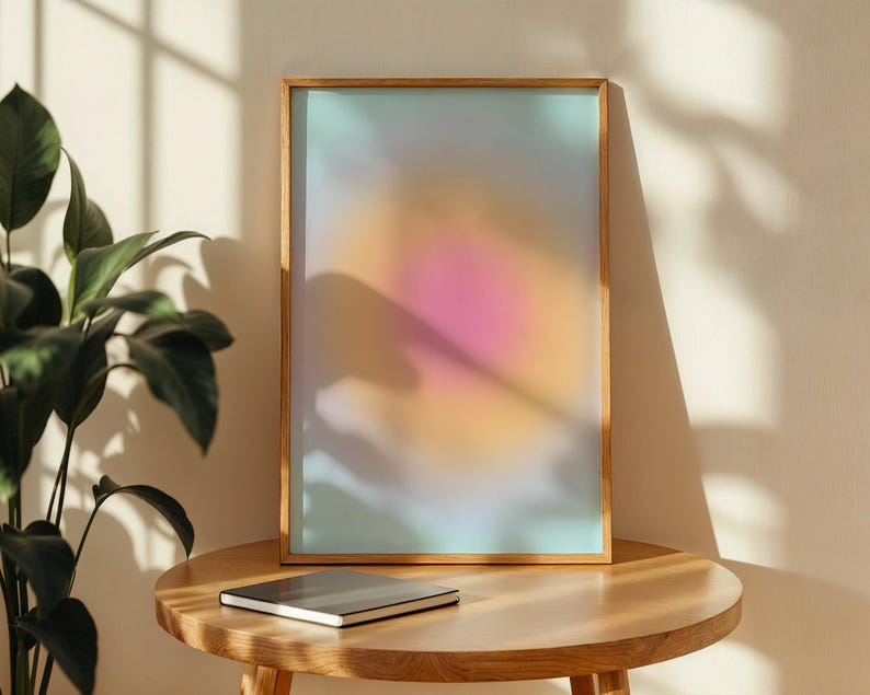 Puede incluir: Una impresi&oacute;n art&iacute;stica enmarcada con un degradado suave y colorido de tonos rosa, naranja y azul. La obra de arte se muestra en un marco de madera natural y descansa sobre una mesa redonda de madera. Un cuaderno cerrado est&aacute; sobre la mesa.