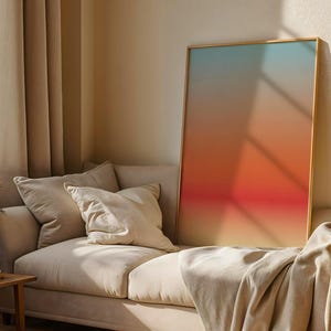 Pode incluir: Uma grande obra de arte emoldurada com um gradiente de cores, do azul ao laranja e ao vermelho, encosta-se a um sofá bege. A sala apresenta cortinas e almofadas bege, criando uma atmosfera acolhedora. Uma mesa lateral de madeira e uma planta decorativa também são visíveis.