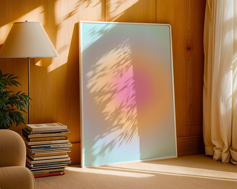 Puede incluir: Una impresi&oacute;n art&iacute;stica enmarcada con un degradado suave y colorido de tonos rosa, naranja y azul. La obra de arte est&aacute; apoyada contra una pared de madera, con sombras de hojas proyectadas sobre ella. Una l&aacute;mpara y una pila de libros est&aacute;n en primer plano.