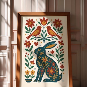 Può includere: Stampa artistica incorniciata con un coniglio turchese con dettagli floreali, circondato da fiori rossi, foglie verdi e due uccelli arancioni. L'opera, su sfondo crema, è racchiusa in una cornice di legno, adatta all'arredamento.