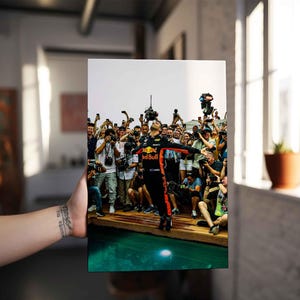 May include: A framed print featuring a Formula 1 driver in a Red Bull racing suit, celebrating with arms outstretched. The image captures a moment of triumph, surrounded by a crowd of cheering fans and photographers.