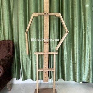 May include: A wooden artist's mannequin with articulated arms and legs, standing on a rectangular base. The mannequin is made of light-colored wood and features a simple, geometric design. The text "RM-replicamuseum" is visible on the mannequin.