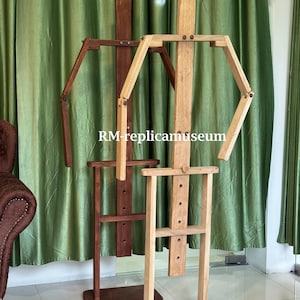 May include: Two wooden artist mannequins. One is a light brown color, and the other is a darker brown. The mannequins have articulated arms and legs, and are standing in front of a green curtain. The text "RM-replicamuseum" is visible.