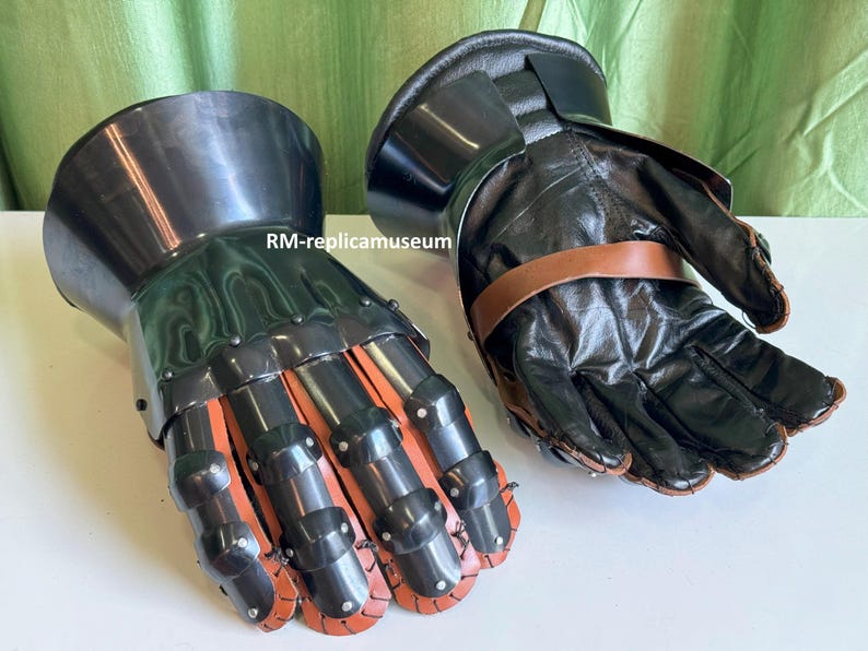 May include: Pair of black and silver medieval gauntlets. The gauntlets feature articulated metal plates over the knuckles and fingers, with red leather accents. The palms and cuffs are made of black leather, secured with brown straps.