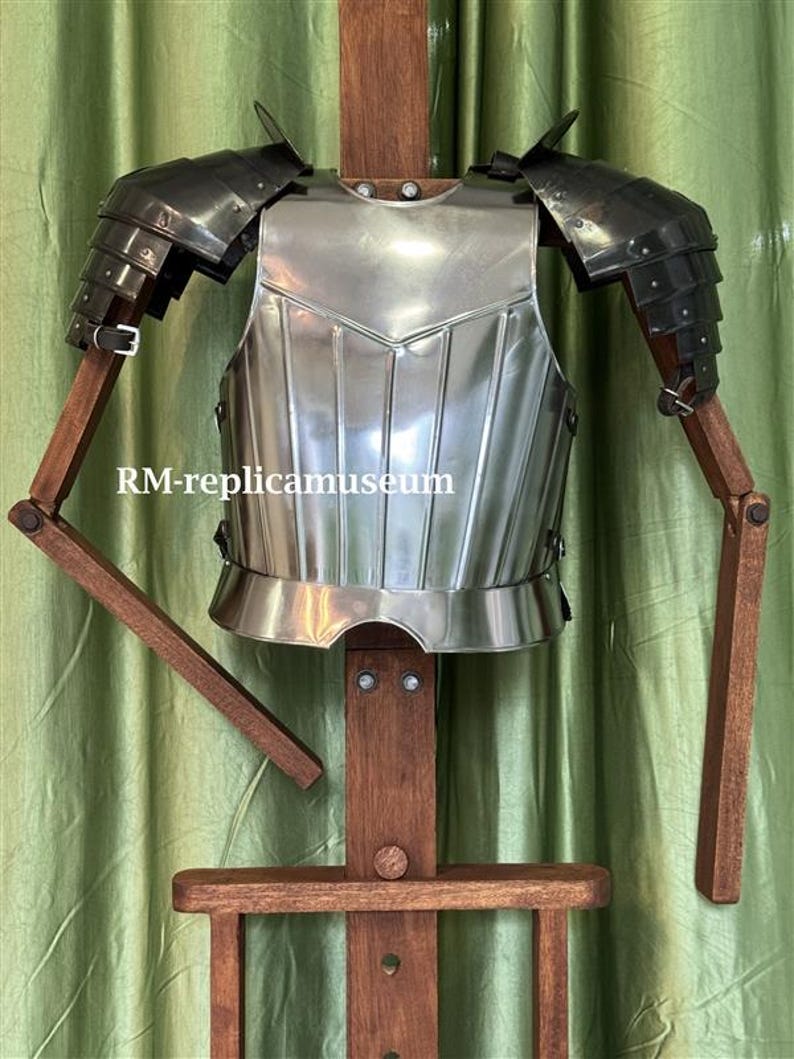 May include: A polished steel breastplate and shoulder armor, displayed on a wooden stand. The armor has a reflective surface and is designed with layered plates. The text "RM-replicamuseum" is visible on the image. The background is a green curtain.
