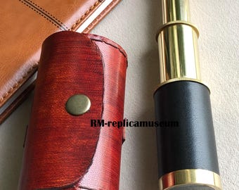 Könnte beinhalten: Ein Messing-Teleskop mit schwarzem Sockel und roter Ledertasche. Das Teleskop befindet sich neben einem braunen Lederjournal. Die Hülle hat einen Messingknopfverschluss. Der Text "DIARY" ist auf dem Journal zu sehen.