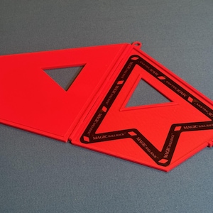 May include: A bright red Magic Ball Rack billiard accessory featuring a hinged, foldable design. The surface displays a triangular cutout and black printed text that reads MAGIC BALL RACK repeatedly along the inner frame edges.