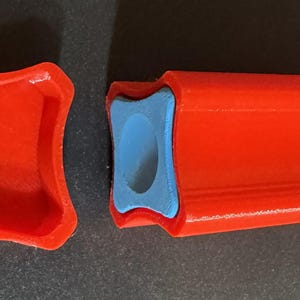 May include: A red 3D-printed object, possibly a container or a part of a larger item, with a blue insert. The object is composed of two parts: a square-shaped lid and a rectangular base. The base has a curved design.