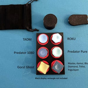May include: A collection of six billiard chalk cubes in various shapes and colors, including light blue, white, purple, mint green, yellow, and grey. The set includes a black velvet drawstring pouch, a round holder, and a clip-on chalk holder.