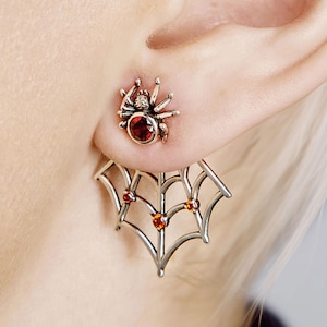 Peut inclure: Boucles d'oreilles araignée en argent avec un clou d'oreille araignée. Le clou d'oreille araignée est de couleur bronze avec une pierre précieuse rouge. Le motif de la toile d'araignée comporte trois pierres précieuses orange.