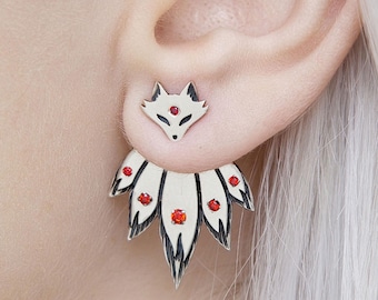 May include: A pair of silver fox earrings with red gemstone accents. The top stud is a fox head, and the back piece features a fan-shaped design with red gems. The earrings are worn on a person's ear.